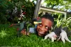 A young boy is playing with dinosaur toys in the grass in front of a house. Náhľad obrázku produktu