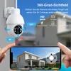 A security camera is shown mounted on a wall, with a smartphone displaying a live feed of a house. Produktbild-Vorschau