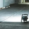 A portable LED work light illuminates a concrete floor in what appears to be a warehouse or industrial setting. Podgląd zdjęcia produktu
