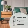 A digital clock with temperature and humidity sensors is displayed on a wooden nightstand next to a sofa. Produktbild-Vorschau