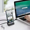 A smartphone is docked in a charging station connected to a laptop, with a hand typing on the laptop keyboard. Podgląd zdjęcia produktu