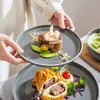 A person is holding a plate with a dessert and another plate with a main course is visible below. Náhled obrázku produktu