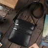 A black leather messenger bag is displayed on a rustic wooden surface, surrounded by other items like glasses and a wooden box. Podgląd zdjęcia produktu