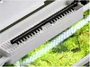 A close-up view of an aquarium setup, showing a black heater or filter component resting on a white plastic tray above lush green aquatic plants and a bright LED light strip. Anteprima dell’immagine prodotto