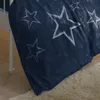 A close-up view of a blue duvet cover with white stars, draped over the edge of a bed. Produktbild-Vorschau
