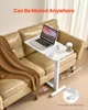 A white mobile laptop table is placed next to a brown leather sofa, with a laptop, glasses, and a coffee cup on it. A brown blanket is draped over the sofa. Podgląd zdjęcia produktu