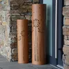 Two decorative outdoor lanterns with a dandelion design are placed on a stone patio next to a stone wall and a glass door. Produktbild-Vorschau