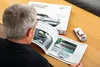 A man is looking at an open book about a Porsche 911 Turbo, with a model car and the product box on a wooden table. Náhled obrázku produktu