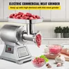 A commercial electric meat grinder is shown on a countertop, with raw meat in the tray and ground meat in bowls. The background is a kitchen setting with cabinets and plants. Náhľad obrázku produktu