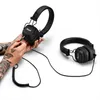 A person's hands with tattoos are plugging a cable into a pair of black Marshall headphones. Another pair of headphones is visible in the background. Náhľad obrázku produktu