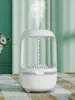 A white humidifier is shown in the center of the image, emitting a mist. The background consists of light green curtains and a patterned rug. Náhled obrázku produktu
