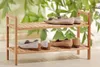 A wooden shoe rack with shoes on it, in front of a leafy green background. Produktbild-Vorschau