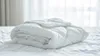 A white comforter is folded and placed on a white bed. Podgląd zdjęcia produktu