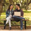 A couple sitting on a park bench with a laptop and books. Produktbild-Vorschau