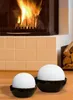 Two white spherical humidifiers in black bowls are placed on a wooden surface in front of a fireplace. Produktbild-Vorschau