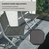 Two KETTLER Basic Plus balcony folding chairs are shown on a tiled patio next to a white brick wall, with greenery visible through a window in the background. A close-up inset shows the texture of the outdoor fabric. Produktbild-Vorschau