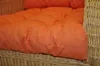 A close-up view of an orange cushion on a wicker chair. Produktbild-Vorschau