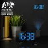 A digital alarm clock with projection is shown on a dark surface, with a plant and books in the background. The clock displays the time, and a projection of the time is visible on the wall. Produktbild-Vorschau