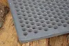 A close-up of a cast iron grate with circular holes, resting on a wooden surface. Náhled obrázku produktu