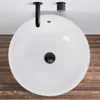 A top-down view of a white round sink with a black drain and a black faucet mounted on the wall above it. The sink is placed on a wooden surface. Anteprima dell’immagine prodotto