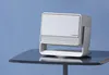 A white and silver projector sits on a dark table against a blue textured background. Náhľad obrázku produktu