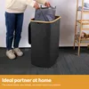 A person is putting a laundry bag into a large, dark gray laundry hamper with a wooden rim. Produktbild-Vorschau