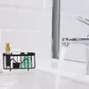 A black wire rack holding a small spray bottle, a tube, and a green sponge sits on the edge of a white sink, with a chrome faucet running water into the sink. Produktbild-Vorschau