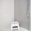 A white folding stool is placed in the corner of a modern shower stall with tiled walls. Produktbild-Vorschau
