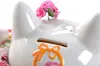 A close-up of a white ceramic Maneki-Neko (lucky cat) piggy bank with pink flowers on top and an orange bow decoration. Podgląd zdjęcia produktu