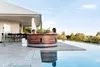 A couple relaxing in a wooden hot tub next to an infinity pool with a scenic view. Náhled obrázku produktu