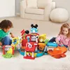 Two young children are playing with a colorful toy car garage playset on a carpeted floor. Produktbild-Vorschau