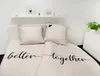 A neatly made bed with beige bedding featuring black text and hearts, set against a white wall with a shelf above. Produktbild-Vorschau