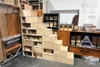 A wooden modular shelving unit designed like stairs, with various compartments and drawers, displayed in what appears to be a workshop or store setting. Produktbild-Vorschau