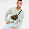 A man wearing a light green sweatshirt and light blue jeans is posing with an olive green Eastpak Springer bum bag across his chest. Produktbild-Vorschau