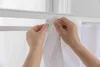 Hands attaching a white curtain to a curtain rod. Produktbild-Vorschau