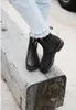 A person wearing light blue jeans and black boots is sitting on a large wooden beam. Náhled obrázku produktu