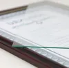 A close-up shot of a wooden picture frame with a certificate inside, partially covered by a clear glass sheet. Produktbild-Vorschau
