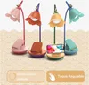 A collage of four desk lamps with flower-shaped shades, each with a phone stand at its base. The lamps are in different colors: pink, orange, yellow, and teal. The background has a decorative pattern. There are also two text boxes with icons. Produktbild-Vorschau