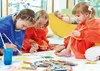 Children are painting on a large sheet of paper on the floor, wearing art smocks. Another child is lying on a yellow beanbag chair in the background. Voir les images du produit