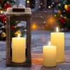 Outdoor LED candles and a wooden lantern are placed on a snowy ground in front of a decorated Christmas tree and a house. Voir les images du produit