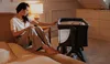 A woman sitting on a bed next to a baby crib. Produktbild-Vorschau