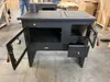 A black wood-burning stove with its doors open, placed in a warehouse or workshop setting. Anteprima dell’immagine prodotto