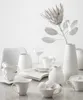 A collection of white ceramic tableware and a decorative dried flower arranged on a marble surface. Produktbild-Vorschau