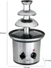A three-tiered chocolate fountain with control knobs and a red indicator light on its base, set against a white background with dimension lines indicating height and width. Podgląd zdjęcia produktu