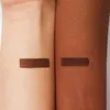 Two arms, one with lighter skin and one with darker skin, are shown with a swatch of dark brown makeup applied to each. Anteprima dell’immagine prodotto