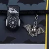 A close-up of a backpack's buckle and a bat-shaped keychain. Voir les images du produit