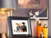 A digital picture frame displaying a couple with a dog, placed on a shelf next to decorative vases and a lamp. Anteprima dell’immagine prodotto