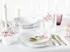 A beautifully set table with white porcelain dinnerware, gold cutlery, and delicate pink flowers. Produktbild-Vorschau