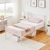 A bedroom scene with a white metal bed frame, pink bedding, and a bedside table. Podgląd zdjęcia produktu