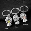 Three silver angel keychains with different colored steering wheels, displayed on a dark, textured surface. Produktbild-Vorschau